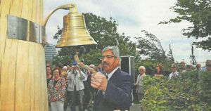 Eine Person läutet eine Glocke an einem Pfahl (Gedenkdalbe) vor zuschauenden Menschen.